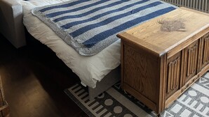 Une chambre à coucher comprenant un lit, des tables de chevet, une armoire en bois, un radiateur et une fenêtre avec des stores.