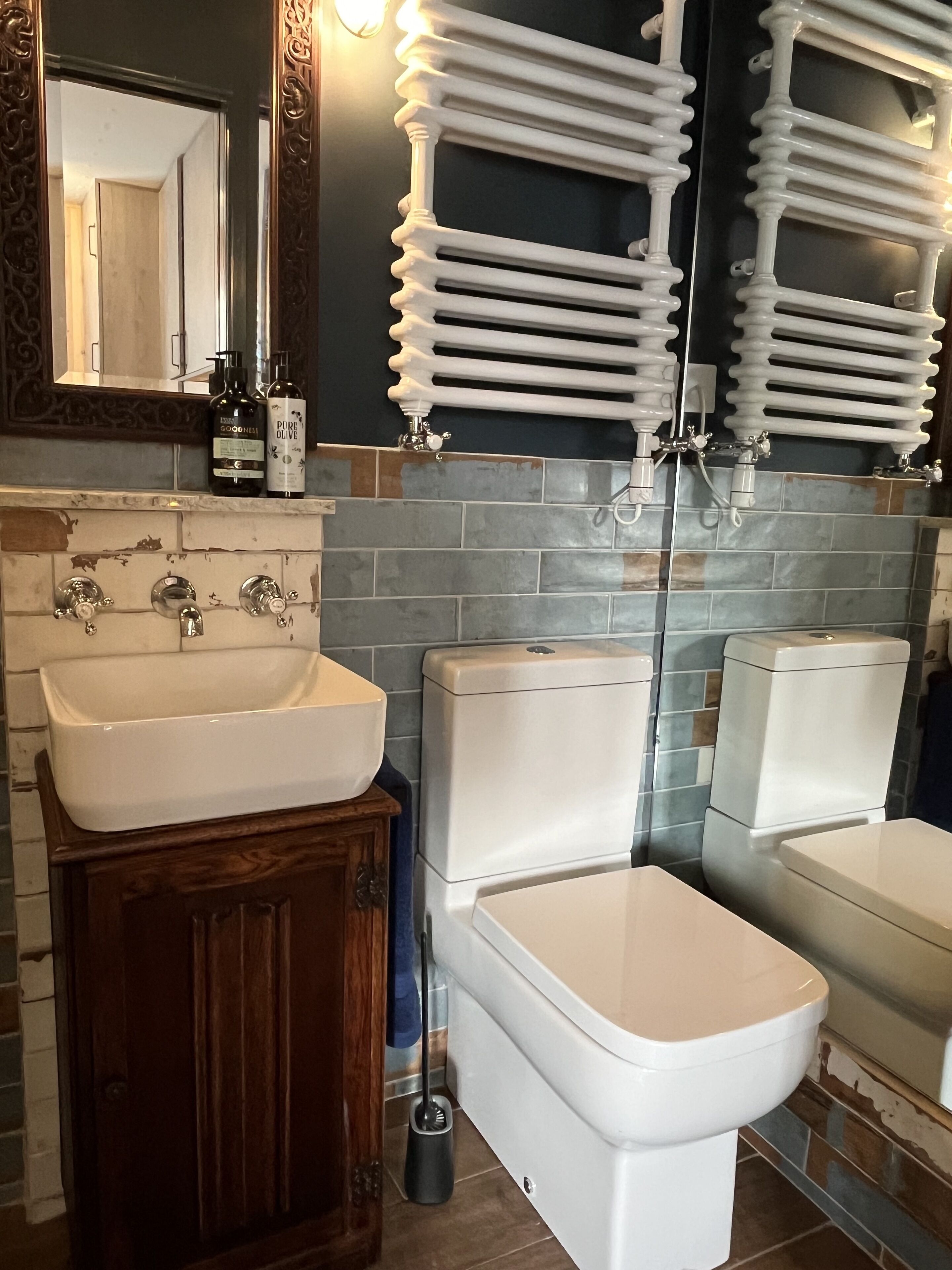 Une salle de bain moderne avec un lavabo blanc, des toilettes et un bidet. Un miroir est placé au-dessus du lavabo et un porte-serviettes au-dessus des toilettes.