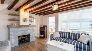A cozy living room with a fireplace, striped sofa, and wooden beams on the ceiling. - Charming Cottage, Private Lake MI Beach (West Olive)