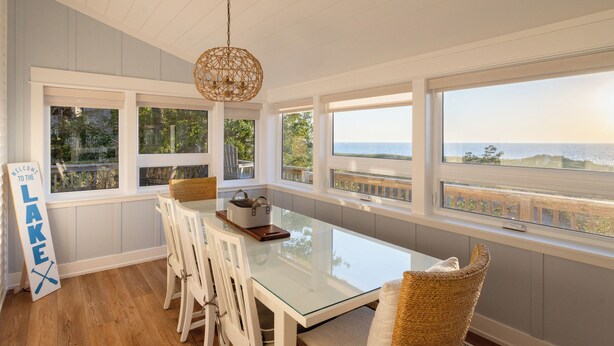 A dining area with a glass table, white chairs, and a view of the sea. - Charming Cottage, Private Lake MI Beach (West Olive)