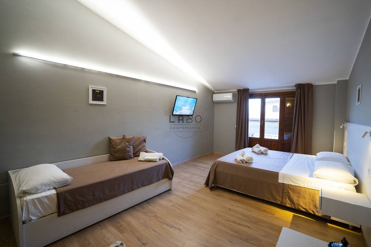A hotel room with two beds, a flat-screen TV mounted on the wall, and an air conditioning unit.