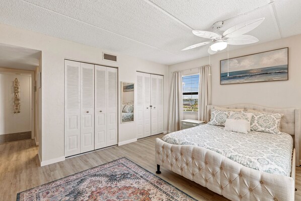 A bedroom with a large bed, a ceiling fan, and a view of the ocean through the window. - ⭐Spacious 2BR-Walk to Beach-Pool + Tennis Courts-Ocean Terrace Club 601⭐ (Daytona Beach)