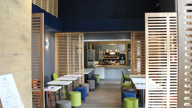 Un interior de restaurante moderno con divisiones de listones de madera, mesas y taburetes de colores.