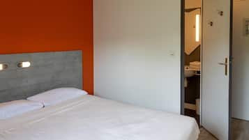 Een hotelkamer met een bed, een hoofdbord, een garderobe en een badkamer die door een open deur zichtbaar is.