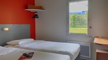 Une chambre d’hôtel avec deux lits, une fenêtre donnant sur l’extérieur, une table de chevet et une lampe.
