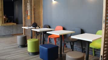 Een modern café met houten lamellen, witte tafels, kleurrijke stoelen en ronde krukken.