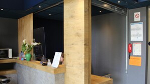 Una mesa de recepción con panel de madera, un florero verde con flores, un microondas y un cubo de basura.