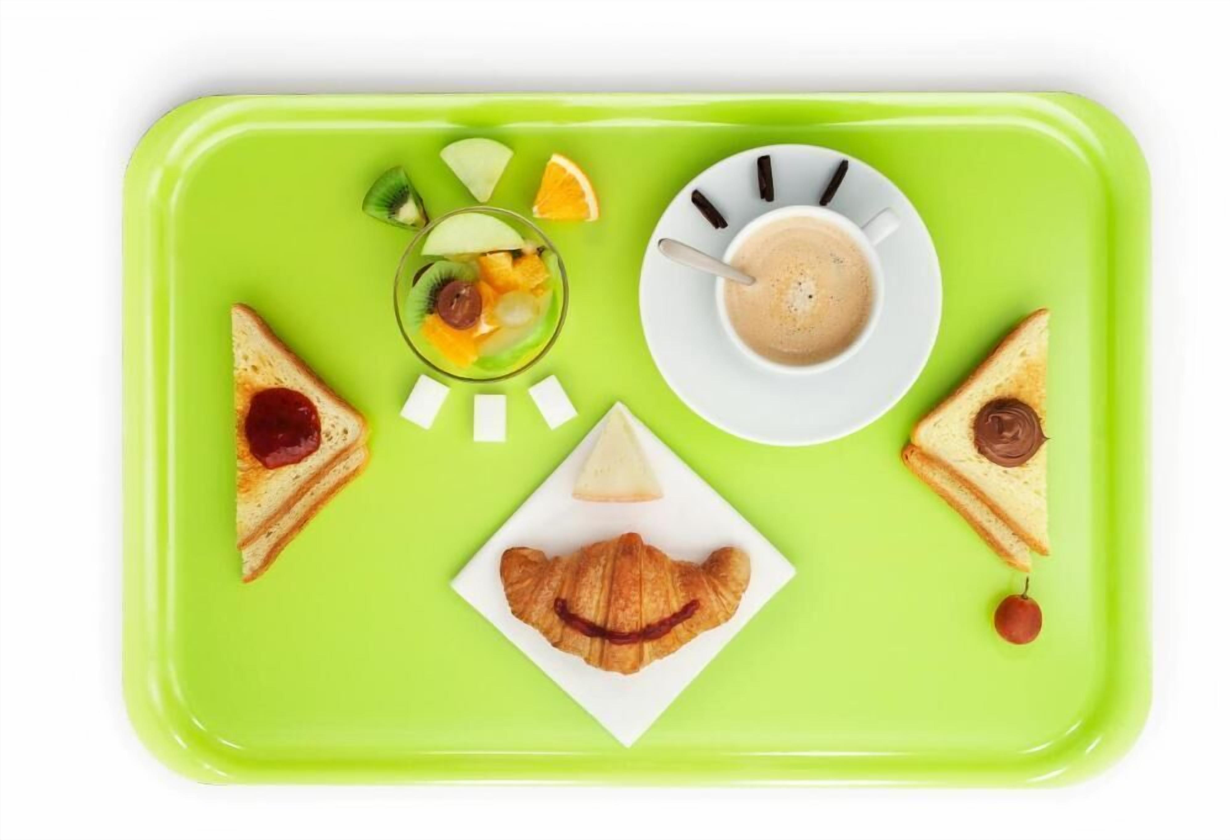 Ein grünes Tablett mit Toast, einem Croissant, einem Glas Fruchtsaft, einer Tasse Kaffee und einer Orangenscheibe.