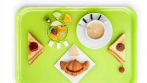Una bandeja verde con tostadas, un croissant, un vaso de jugo de fruta, una taza de café y una rebanada de naranja.