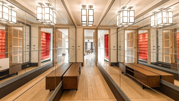 Un couloir d’hôtel moderne avec des murs recouverts de miroirs, des bancs en bois et une allée centrale.