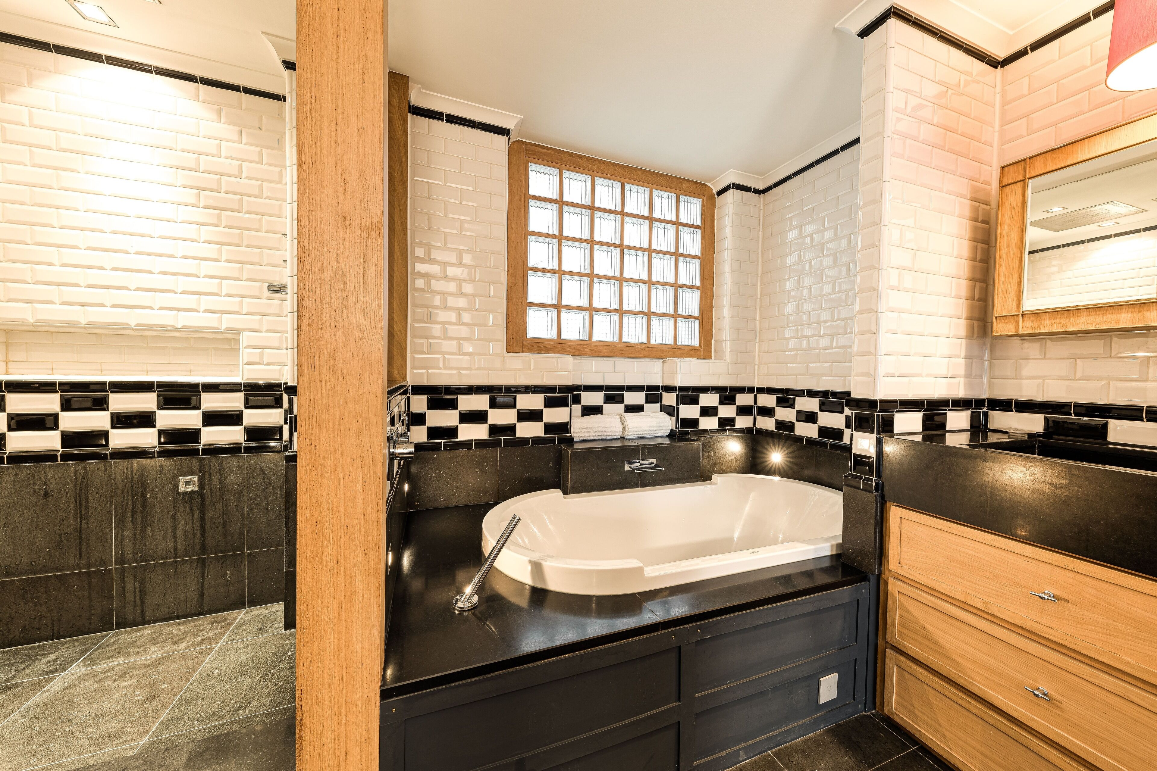 Une salle de bain moderne avec un mur recouvert de carreaux noirs et blancs, une grande fenêtre et un plan de toilette noir.