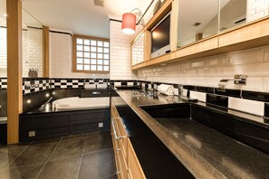 Een moderne badkamer met een zwart-wit geruite vloer, een ruime badkuip en een houten wastafelmeubel met spiegel.