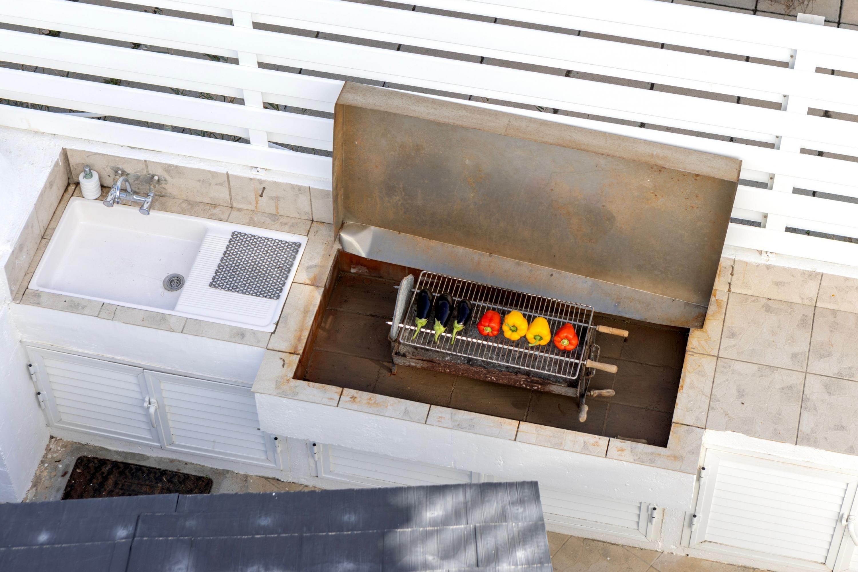 An outdoor kitchen with a grill, a sink, and a white fence.