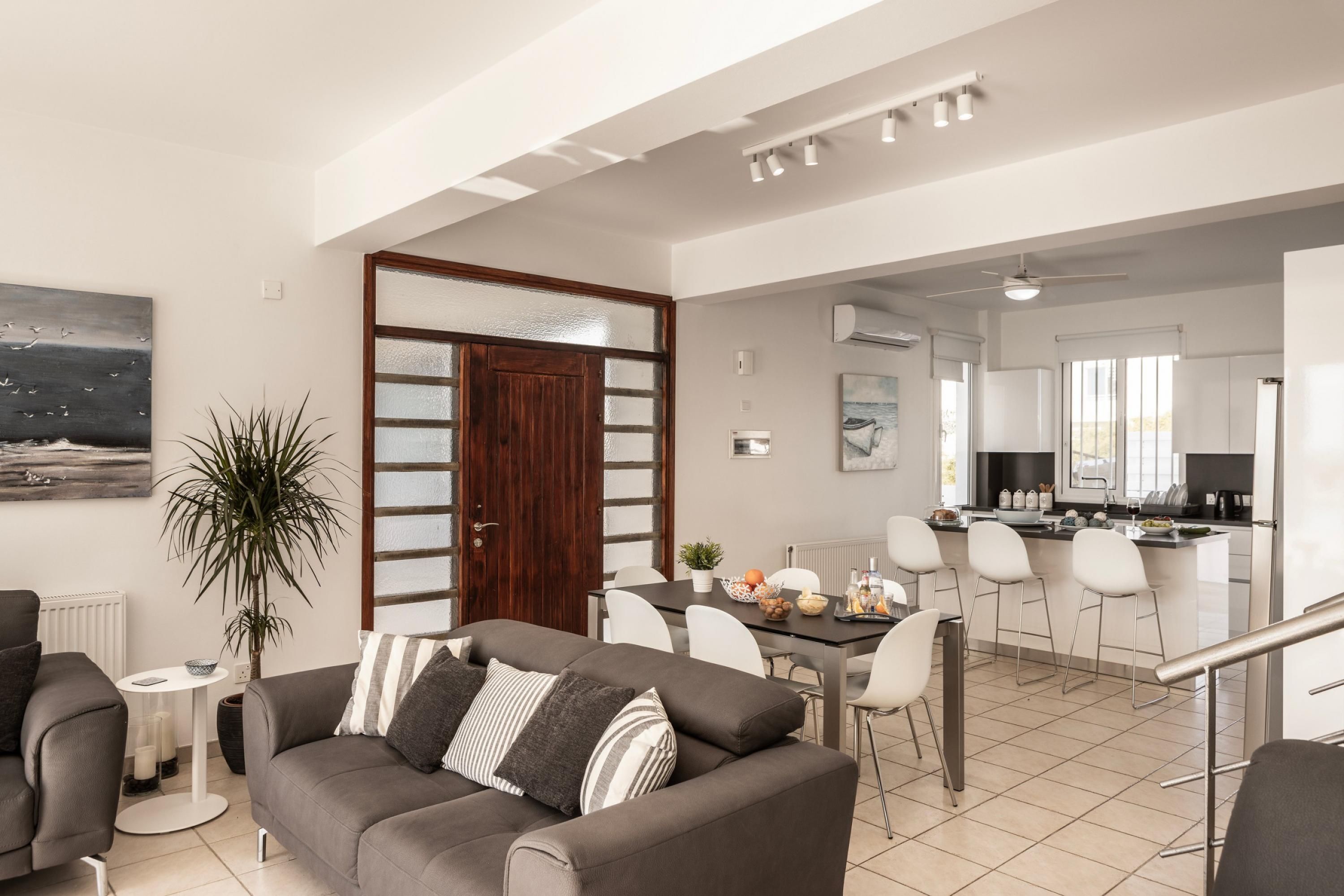 A modern living room with a grey sofa, a dining area with a table and chairs, and a kitchen in the background.