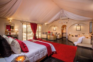 Une pièce spacieuse aménagée sous une tente, avec un grand lit, un coin salon et une salle de bain.