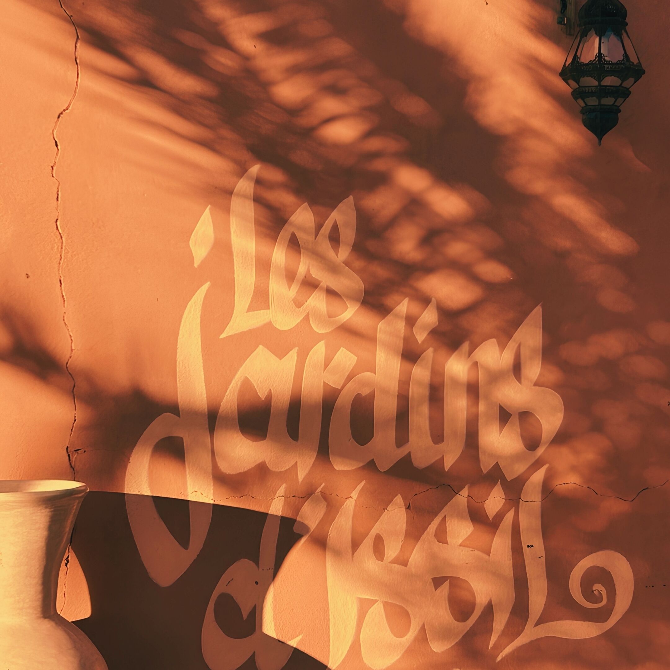 A wall with the text "Les Jardins de l'Hotel" and a lantern.