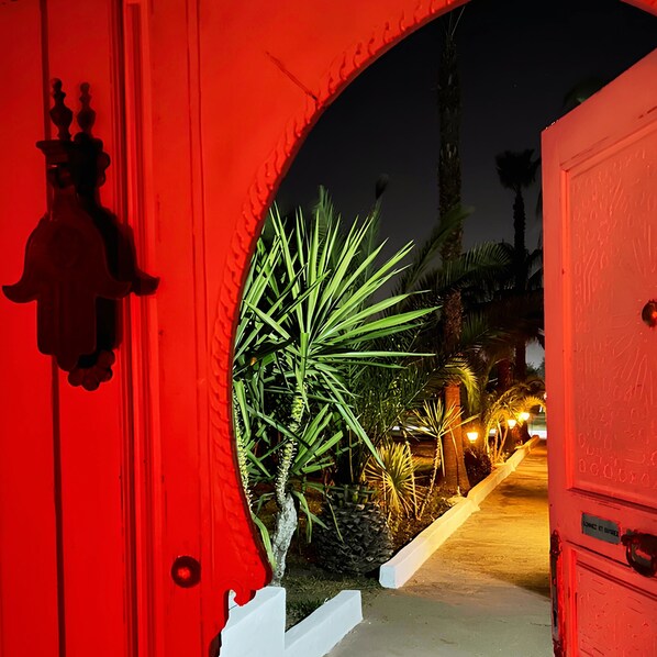Un arc rouge qui mène à un sentier bordé de palmiers, le tout dans une ambiance nocturne.