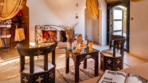 A cozy room with a sloped ceiling, a decorative wall lamp, a framed picture, a small table with a vase, and two chairs. - Les Jardins D'Issil Maison d'Hôtes (Sidi Abdallah Ghiat)