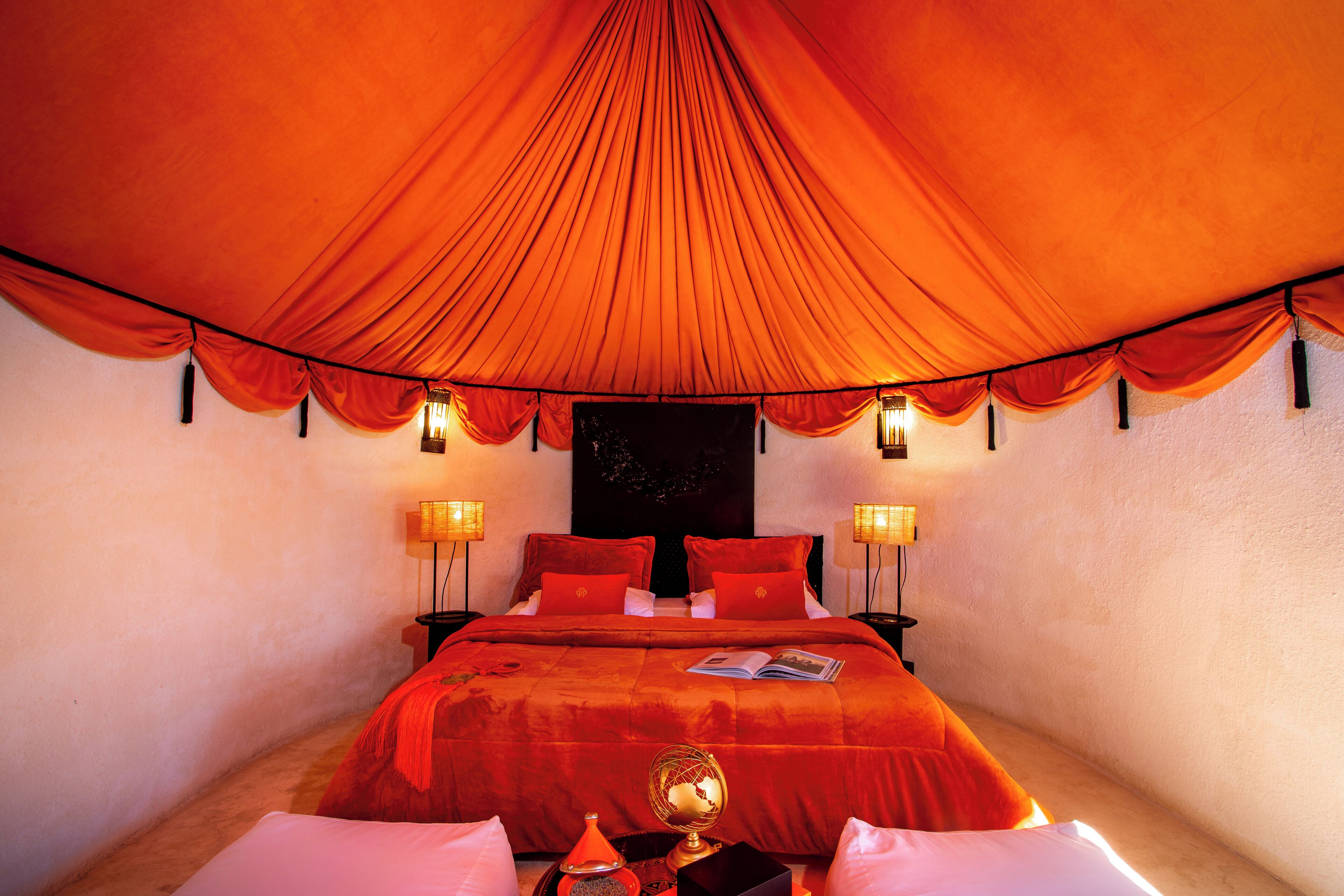 Une chambre avec un grand lit, deux tables de chevet avec des lampes et un baldaquin rouge.