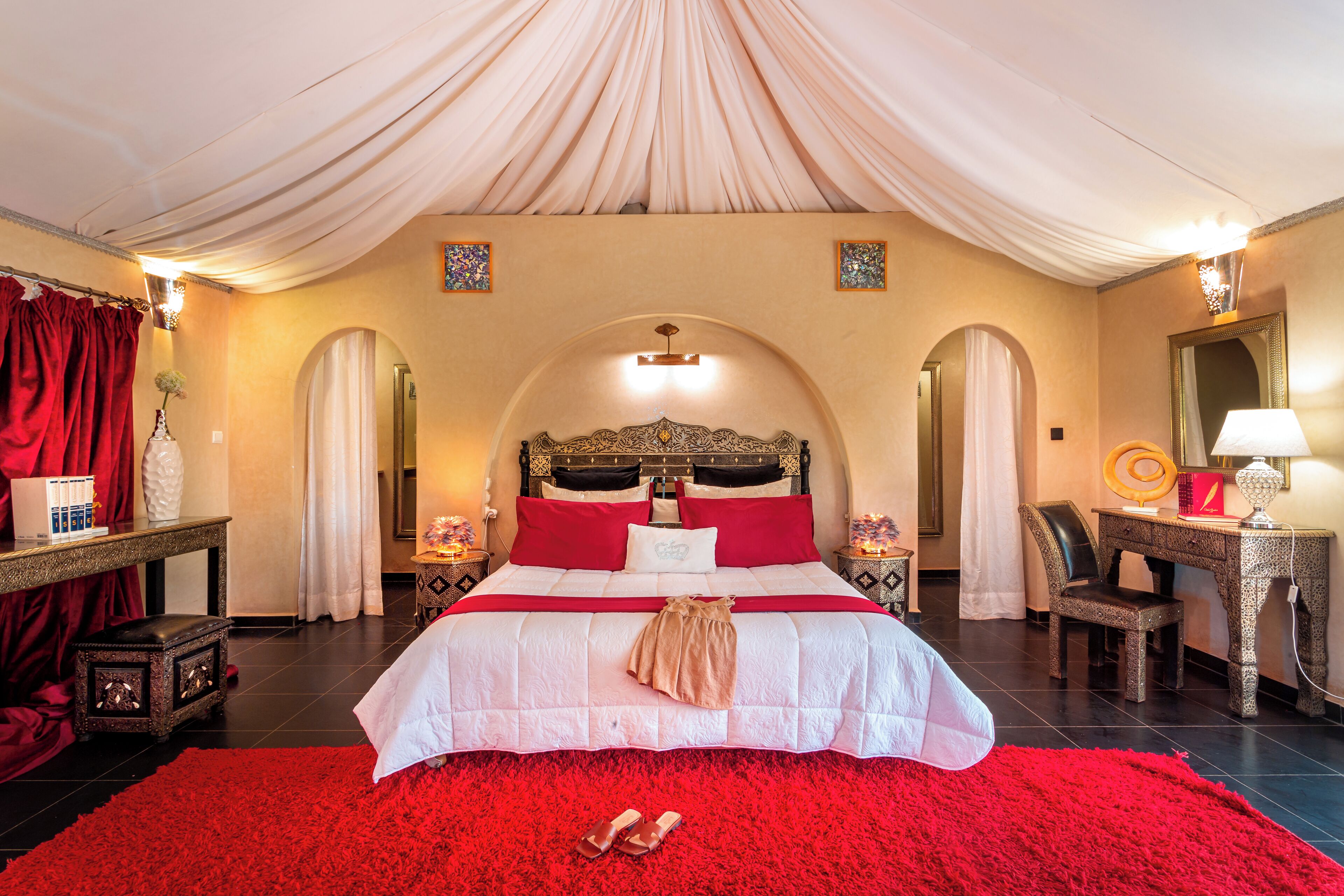 Un dormitorio amplio con una cama grande, cortinas rojas y un candelabro.