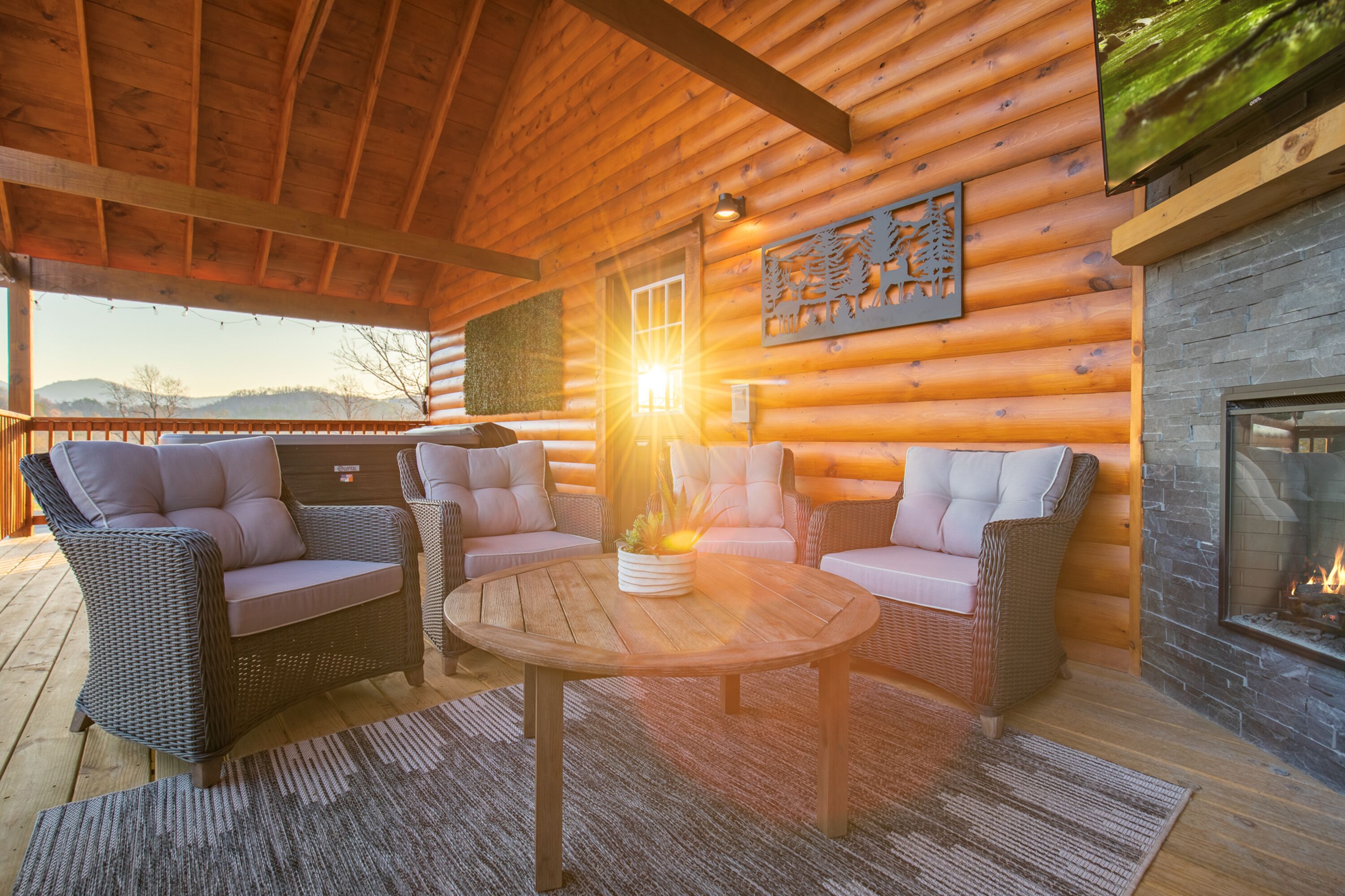 A log cabin interior with wicker furniture, a stone fireplace, and a view of the outdoors.