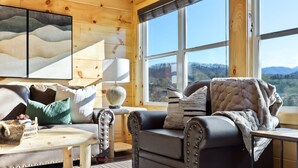 Un salon chaleureux avec un canapé en cuir, une petite table et une vue sur les montagnes grâce à de grandes fenêtres.