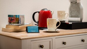 A coffee station with a red coffee maker, two white cups, a book, and a business card on a wooden counter. - Onda Suite (Cagliari)