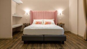 A modern hotel room with a large bed, two bedside tables, a built-in bench, and a wall-mounted shelf. - Onda Suite (Cagliari)