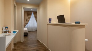 A hotel reception area with a desk, a laptop, and a sign. There is a hallway leading to a room with a bed and curtains. - Onda Suite (Cagliari)