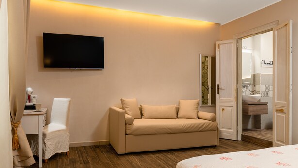 A hotel room with a sofa, a TV mounted on the wall, a desk with a chair, and a bed. - Onda Suite (Cagliari)