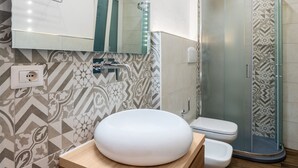 A bathroom with a wooden vanity, a white sink, a toilet, and a glass shower enclosure. - Onda Suite (Cagliari)