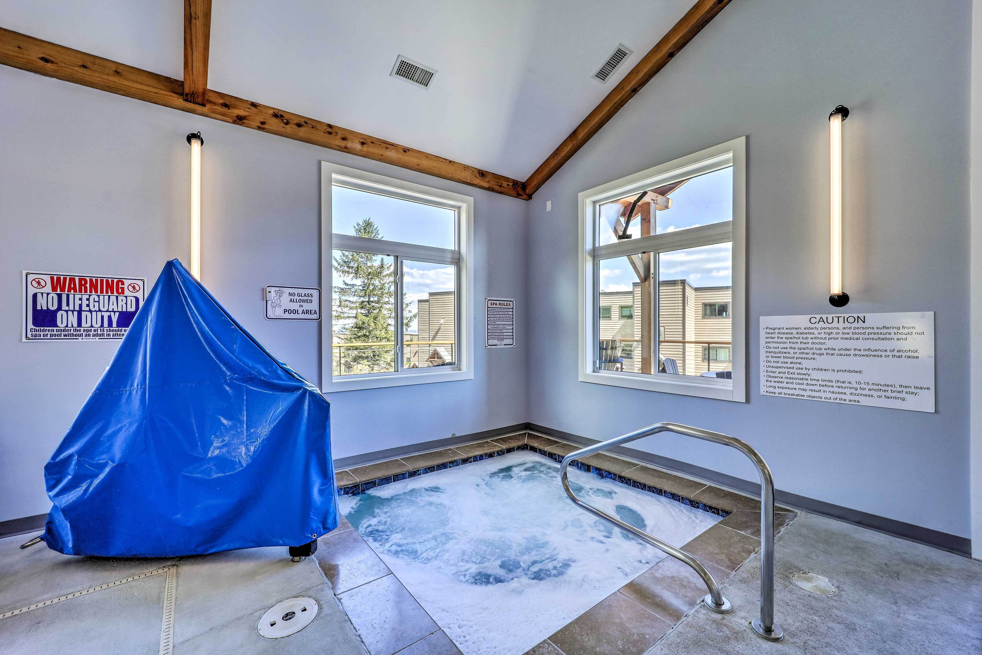 A room with a hot tub, wooden beams, and windows with views of buildings.