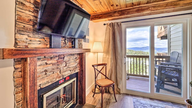 A cozy living room with a stone fireplace, a flat-screen TV mounted above it, and a large sliding glass door leading to an outdoor deck.