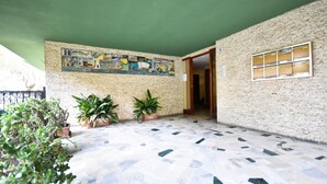 A spacious indoor area with a tiled floor, green walls, and a mural depicting maritime scenes. There are potted plants and a door leading to another room. - Relax Apartment N 5 by Wonderful Italy (Sanremo)