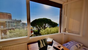 A room with a window overlooking a tree and a building. There is a desk with a laptop, a book, and a phone. - Relax Apartment N 5 by Wonderful Italy (Sanremo)