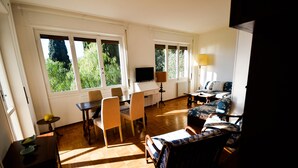 A spacious living room with a wooden floor, large windows, a TV, a desk, and a sofa. - Relax Apartment N 5 by Wonderful Italy (Sanremo)