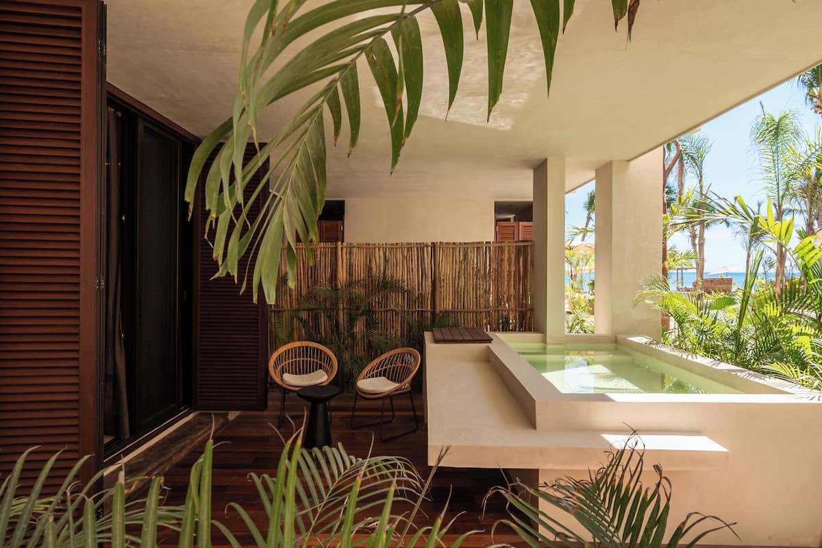 A modern outdoor seating area with a pool, surrounded by tropical plants and a bamboo fence.
