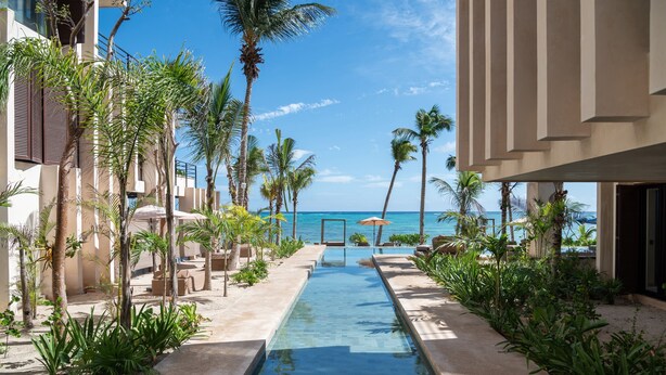 A pool area with a clear view of the ocean, surrounded by palm trees and lounge chairs.