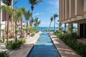 A pool area with a clear view of the ocean, surrounded by palm trees and lounge chairs.