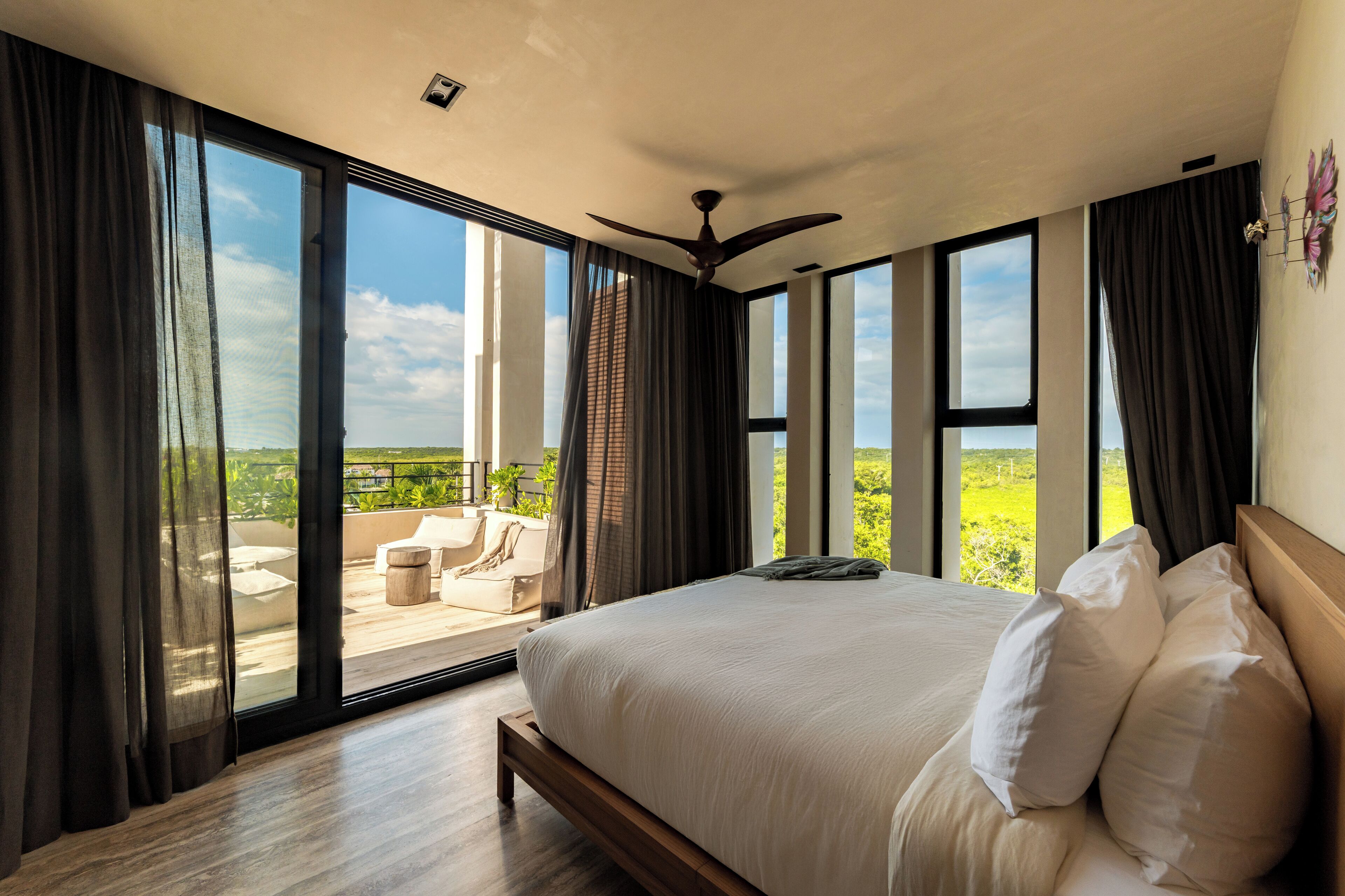 A bedroom with a large bed, a ceiling fan, and a view of a balcony with outdoor furniture.
