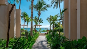 A pathway leading to a beach area with palm trees and umbrellas.
