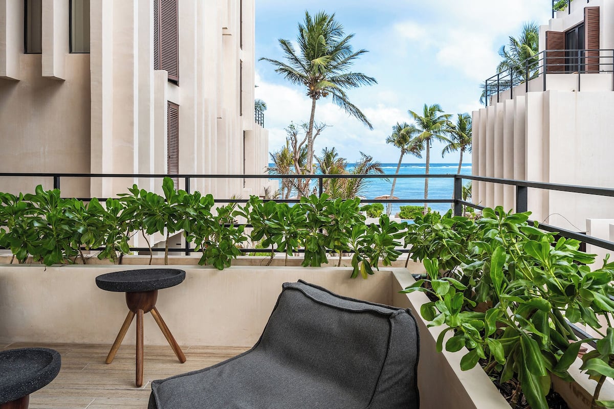 A balcony with a view of the ocean, surrounded by palm trees and a modern building facade.