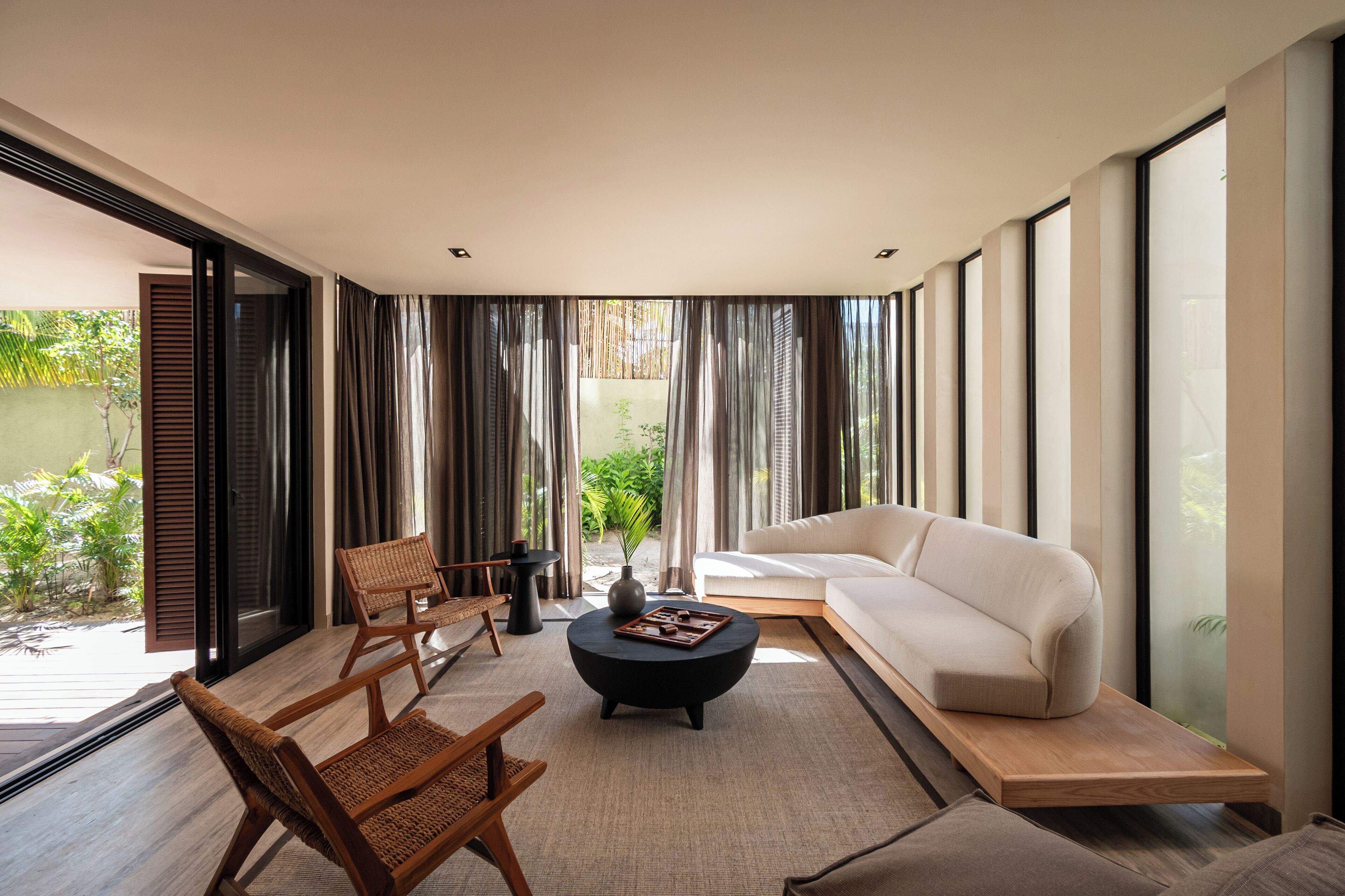 A modern living room with a sofa, two chairs, a coffee table, and large windows.