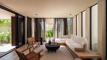 A modern living room with a sofa, two chairs, a coffee table, and large windows.