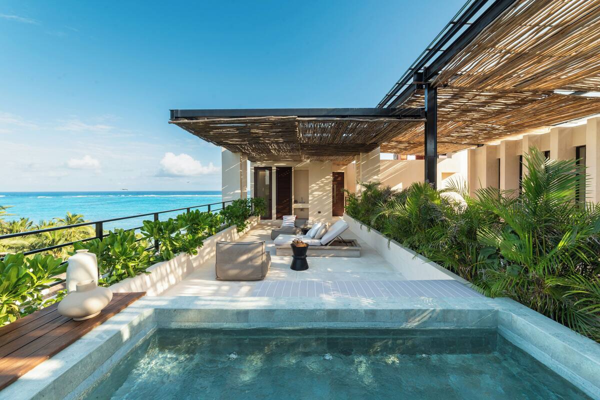 A rooftop infinity pool with a view of the ocean, lounge chairs, and a pergola.
