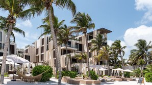 A beachfront hotel with multiple balconies, palm trees, and outdoor seating areas.