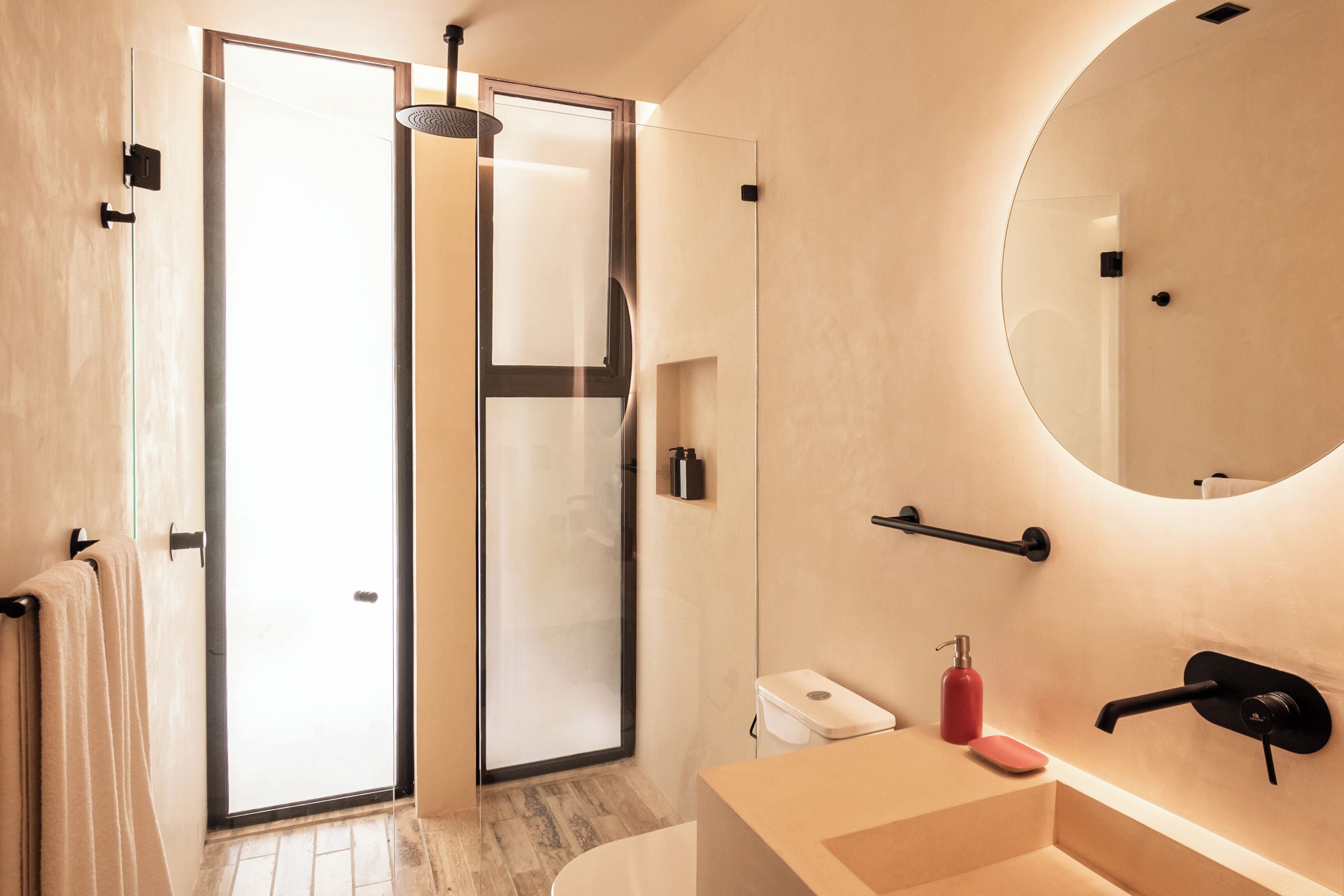 A modern bathroom with a glass shower door, a round mirror, and a beige sink.