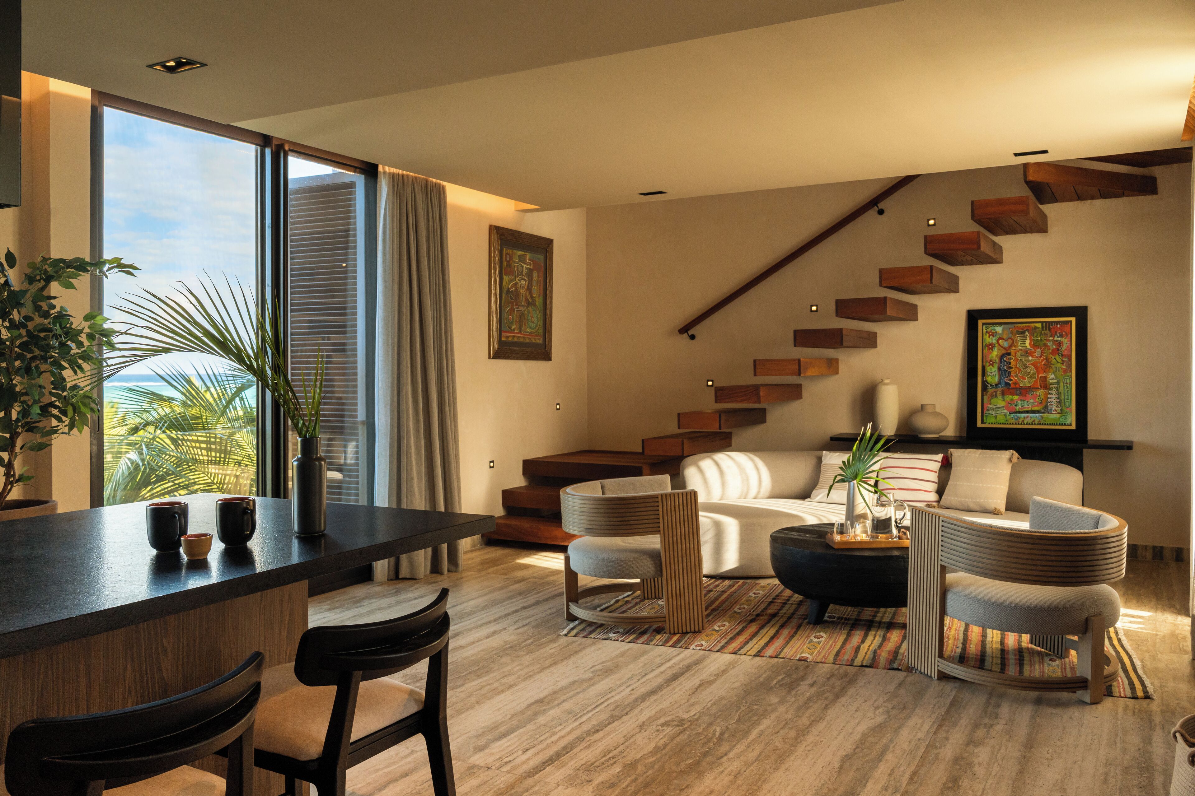 Een moderne woonkamer met een houten trap, een bank, een salontafel en een eetgedeelte met stoelen en een bar.