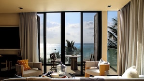 A modern hotel room with a balcony overlooking the sea, furnished with a sofa, chairs, and a table.