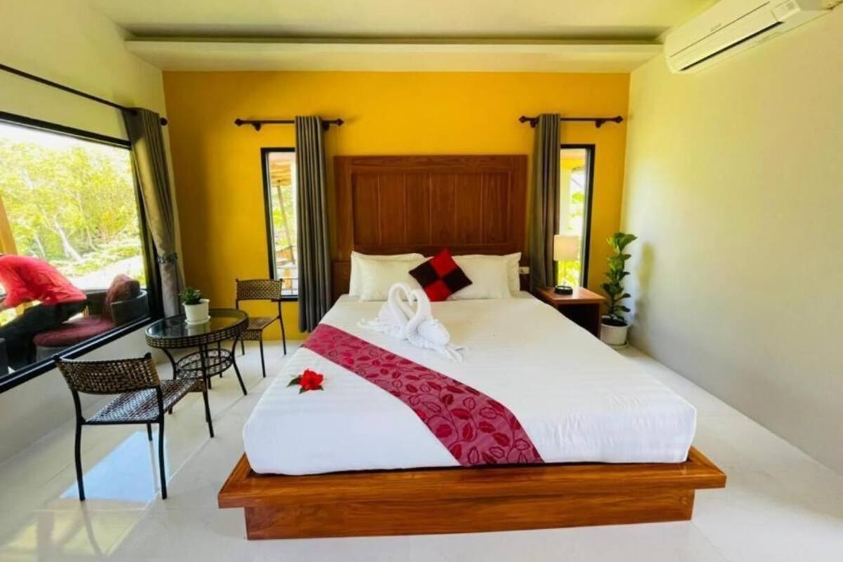 A hotel room with a large bed, a small table, two chairs, and a window with curtains.
